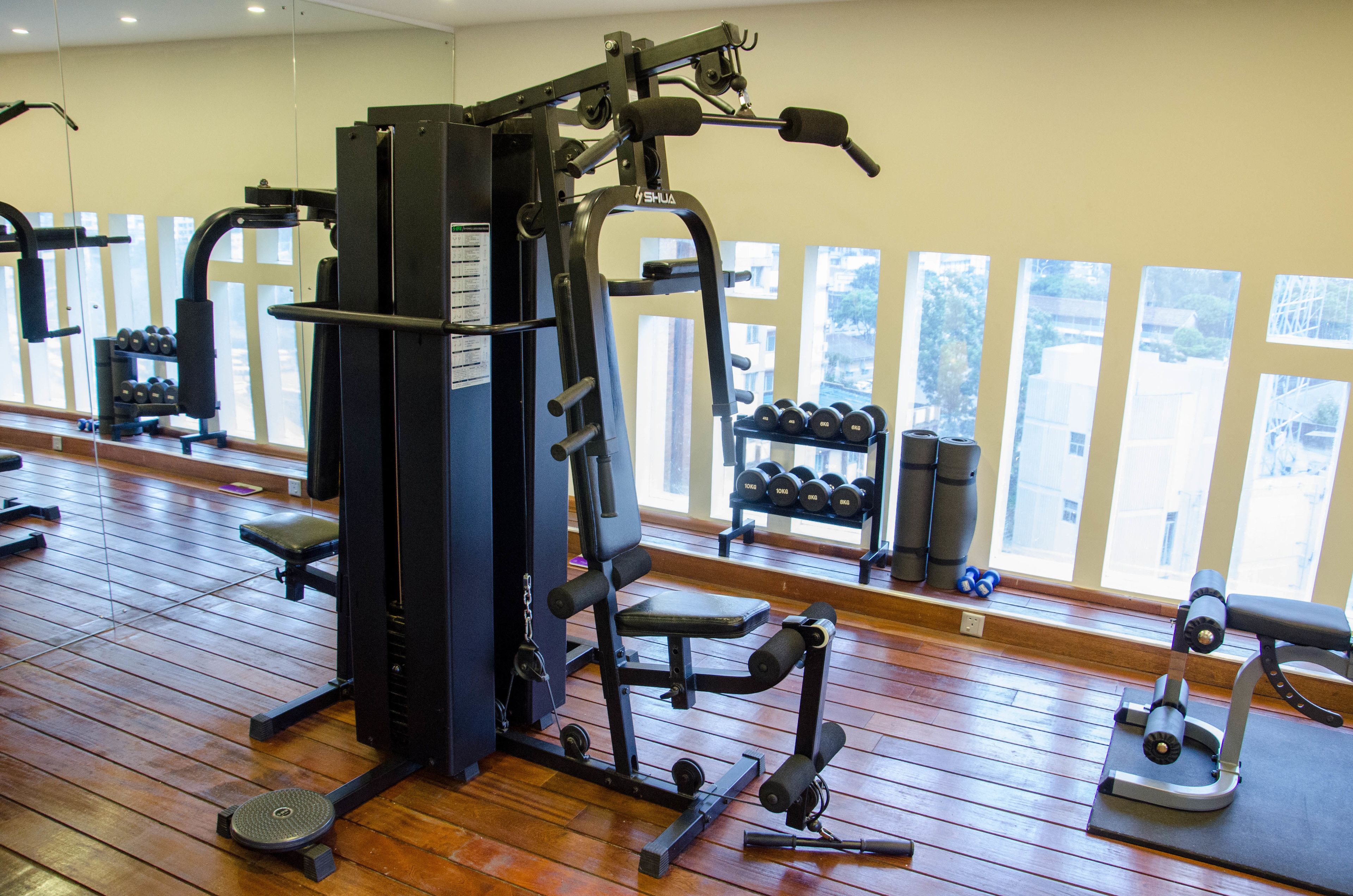 A gym with exercise equipment, wooden flooring, and large windows with a view of buildings.