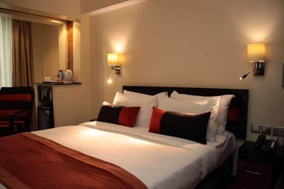 A hotel room with a large bed, two bedside lamps, a nightstand, a chair, and a mirror.