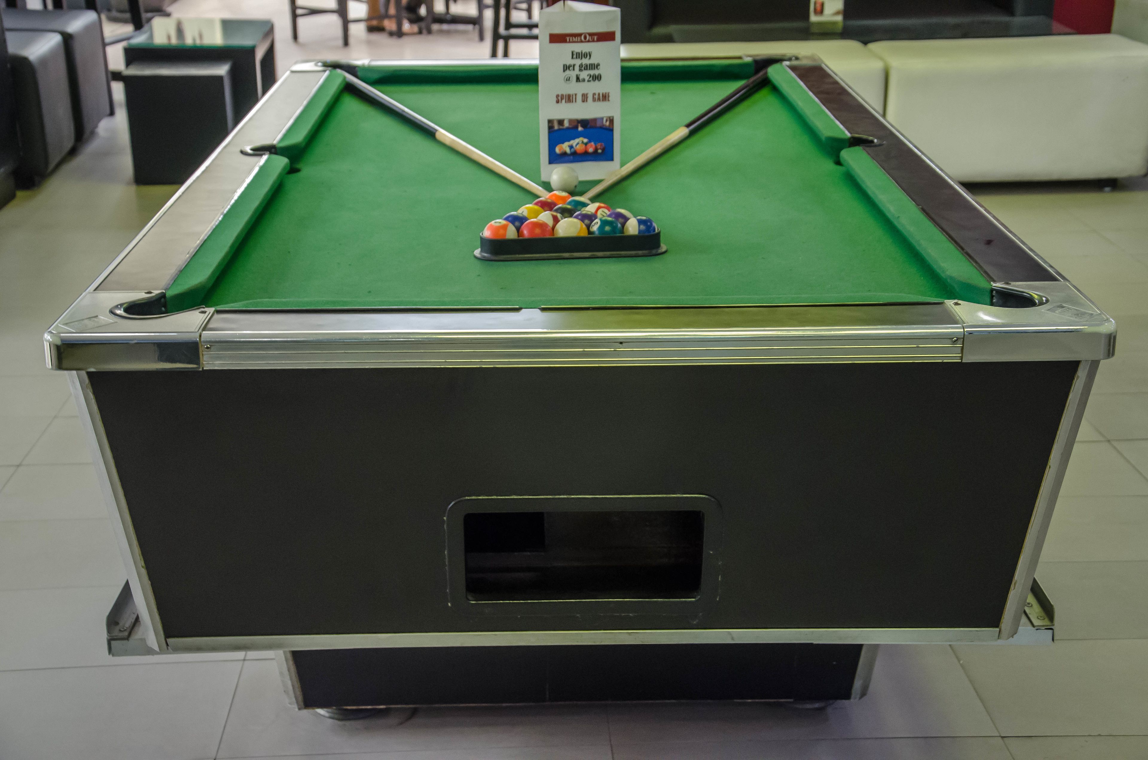 A pool table with a cue ball and billiard balls, a sign indicating a $200 per game rate, and a small window on the table's side.