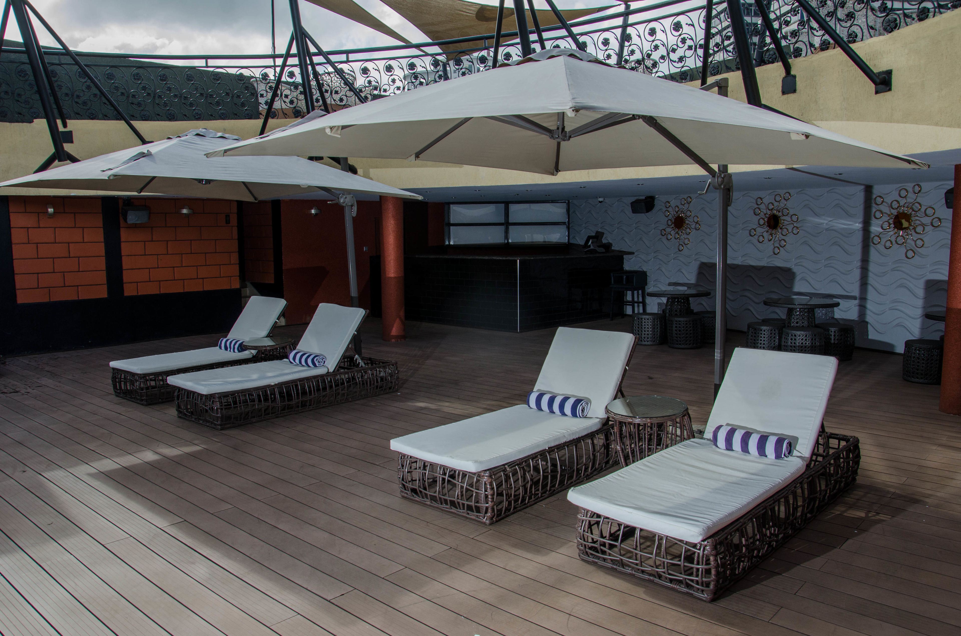A rooftop lounge area with wicker lounge chairs, white umbrellas, and a bar area.