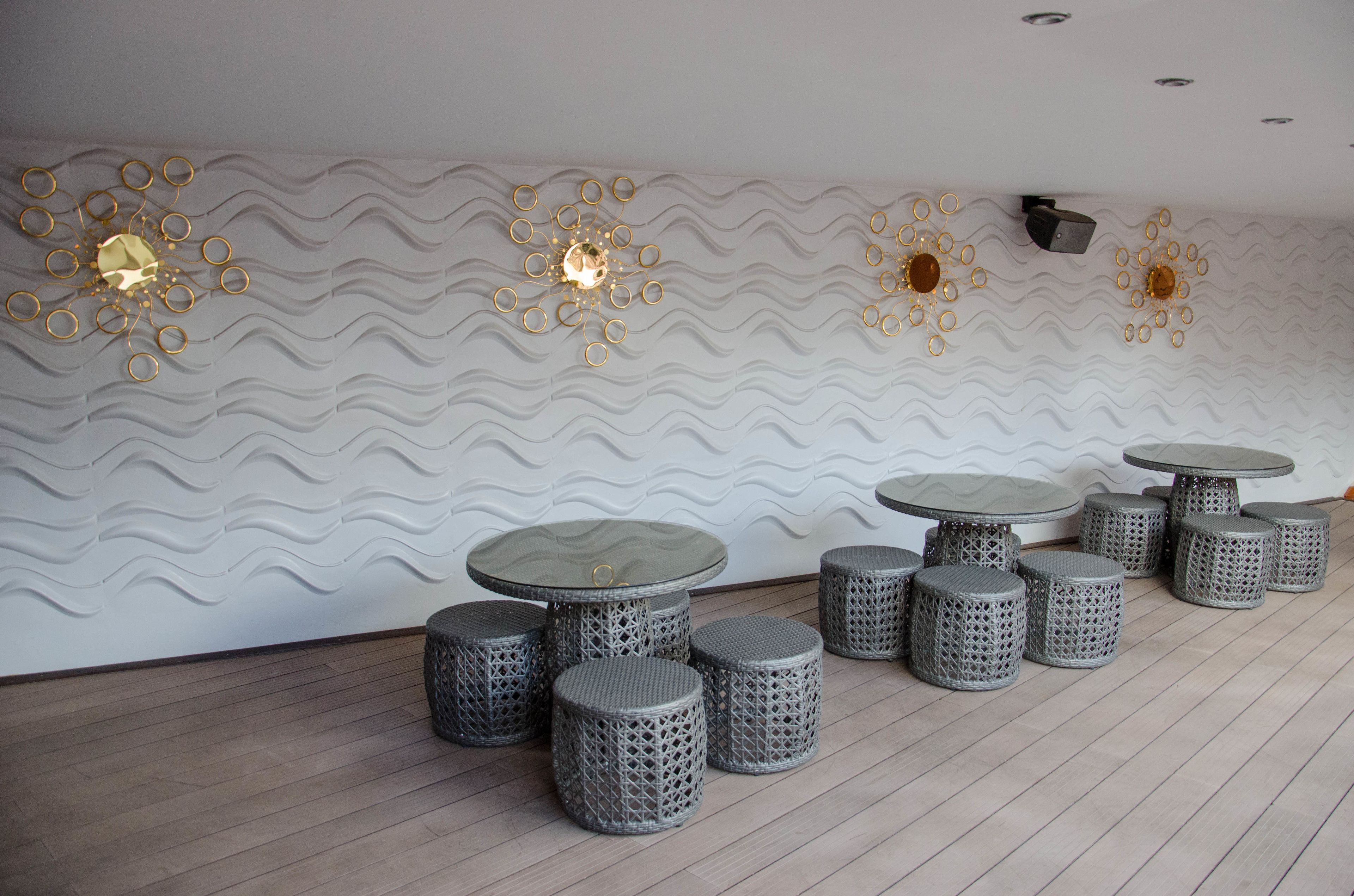 A modern interior with a wavy wall design, multiple round tables, and stools.