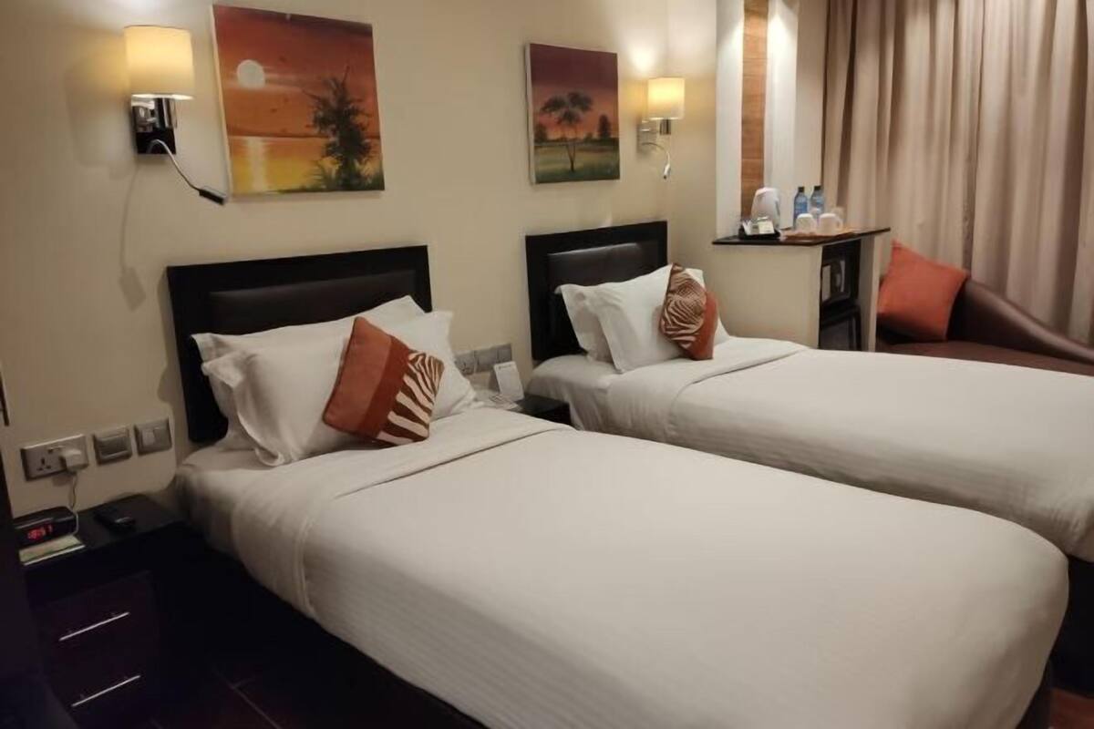 Une chambre d’hôtel avec deux lits, une table de chevet avec une horloge et une petite table avec une lampe et des bouteilles d’eau.