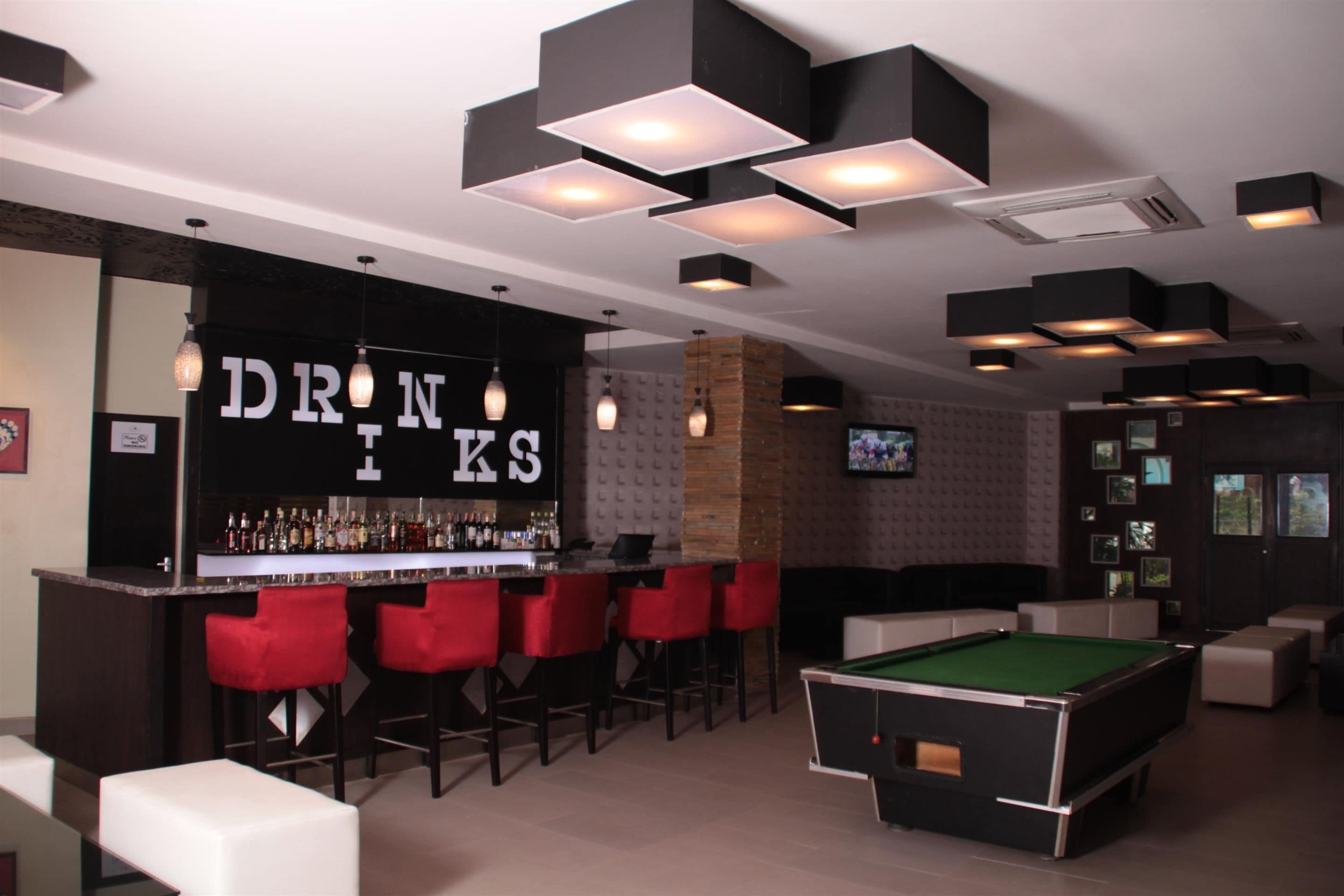 Un espace bar avec un billard, des tabourets de bar rouges et une enseigne indiquant « Boissons ».