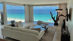 A spacious living room with a large white sofa, a coffee table, and a view of the ocean through floor-to-ceiling windows. - Royal Zanzibar Beach Resort All Inclusive (Nungwi)