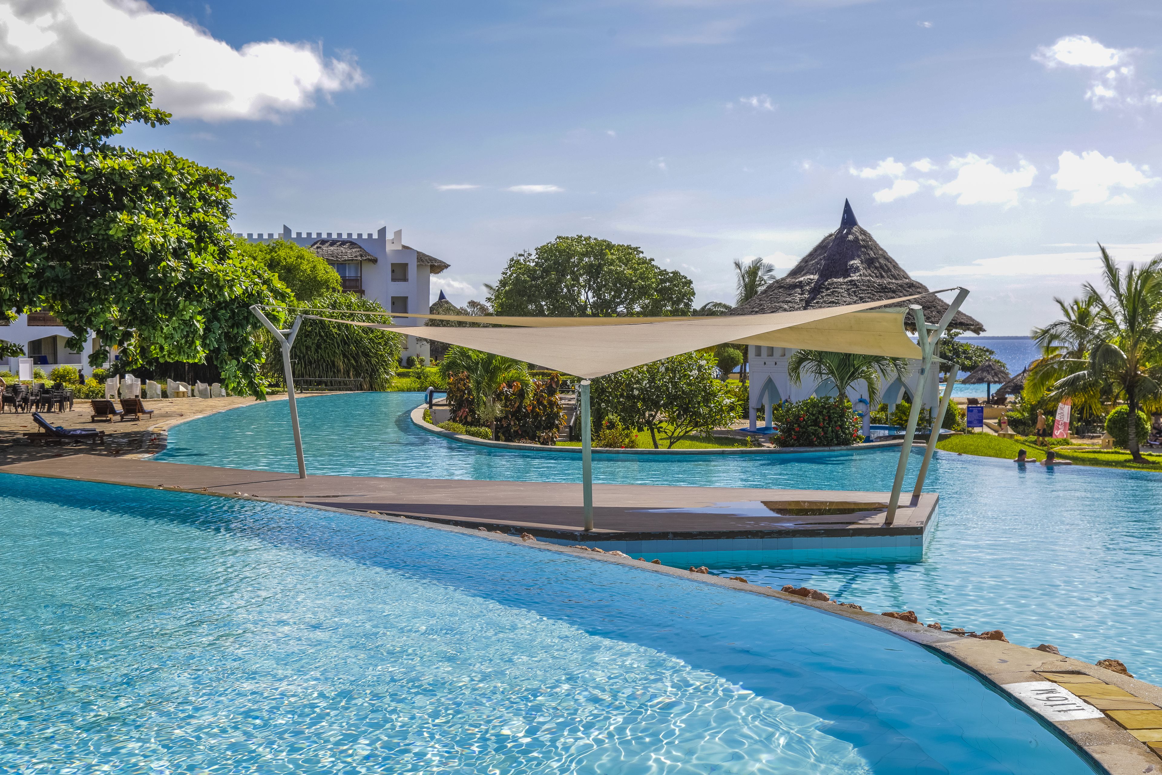 A swimming pool with a curved design, surrounded by lounge chairs and a shaded area.