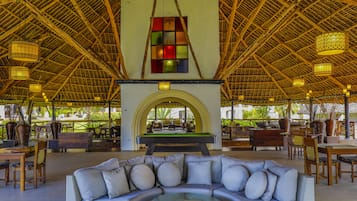 A spacious lounge area with a pool table, comfortable seating, and a high thatched ceiling.