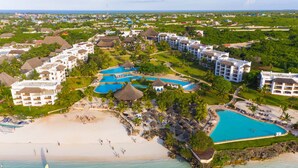 Vue aérienne d’un complexe hôtelier doté de plusieurs piscines, d’une plage et d’une végétation luxuriante.