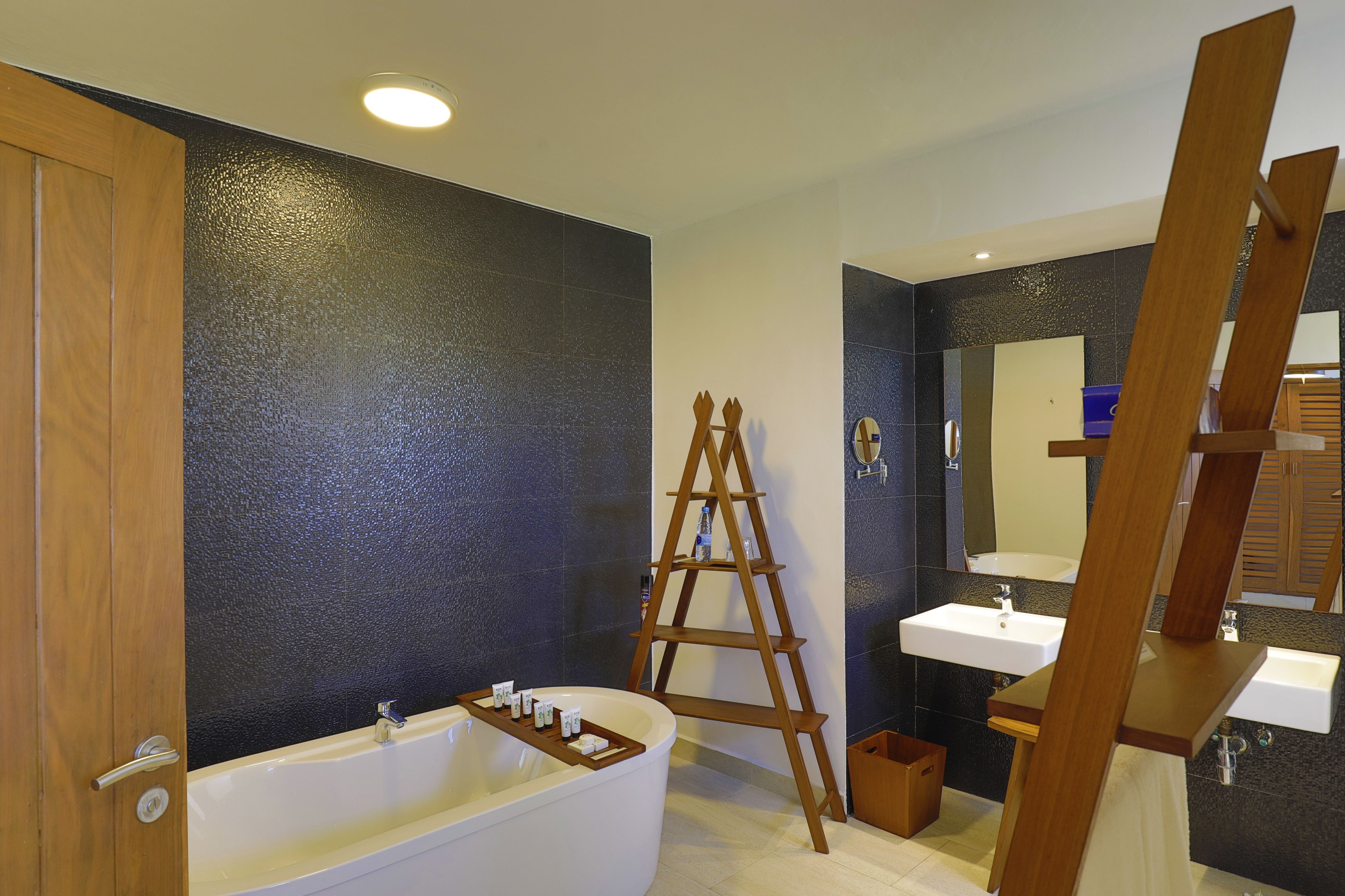 A modern bathroom with a bathtub, two sinks, a wooden ladder, and a large mirror.