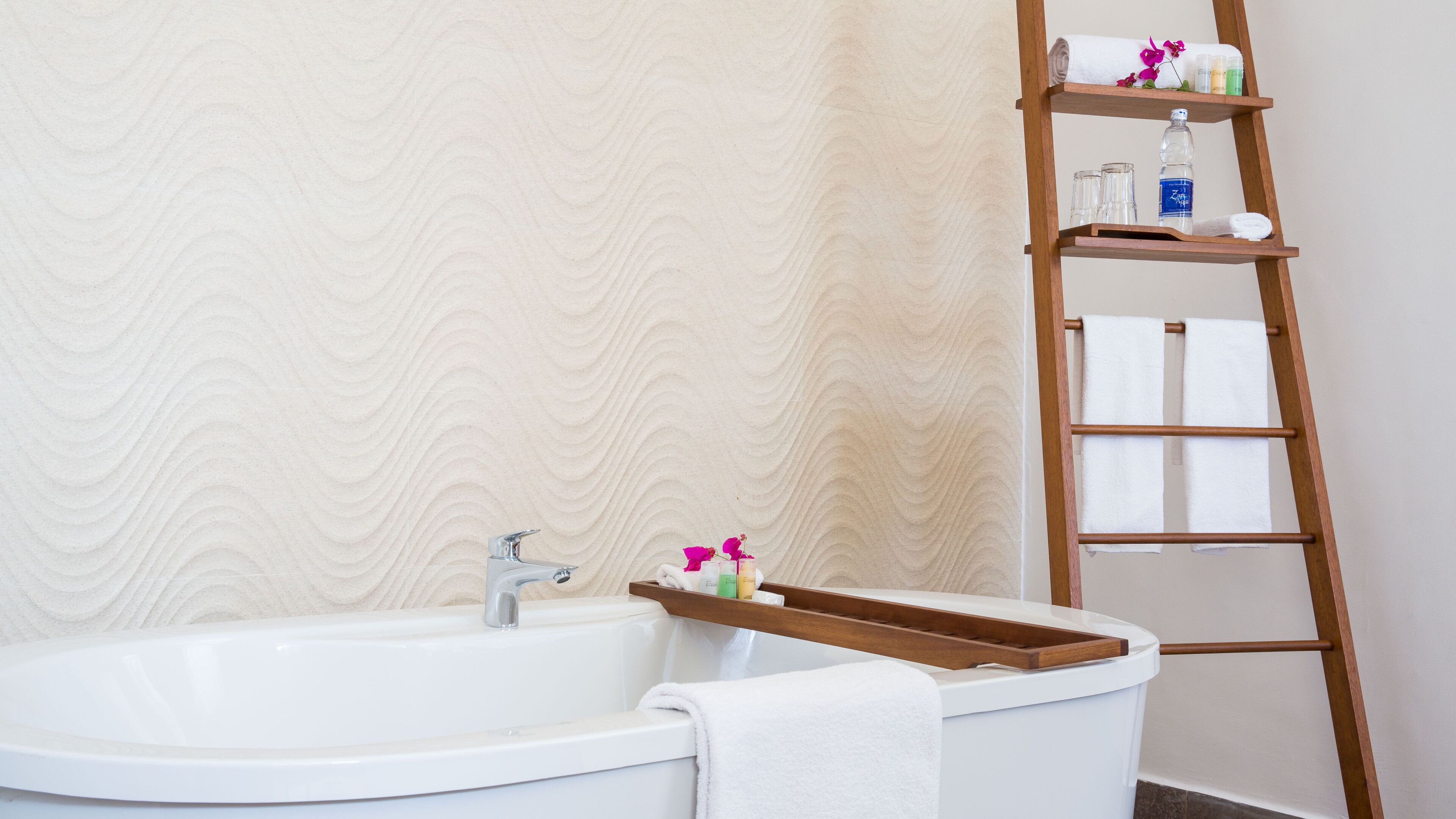 A bathroom with a bathtub, a wooden shelf with toiletries, and a towel rack.
