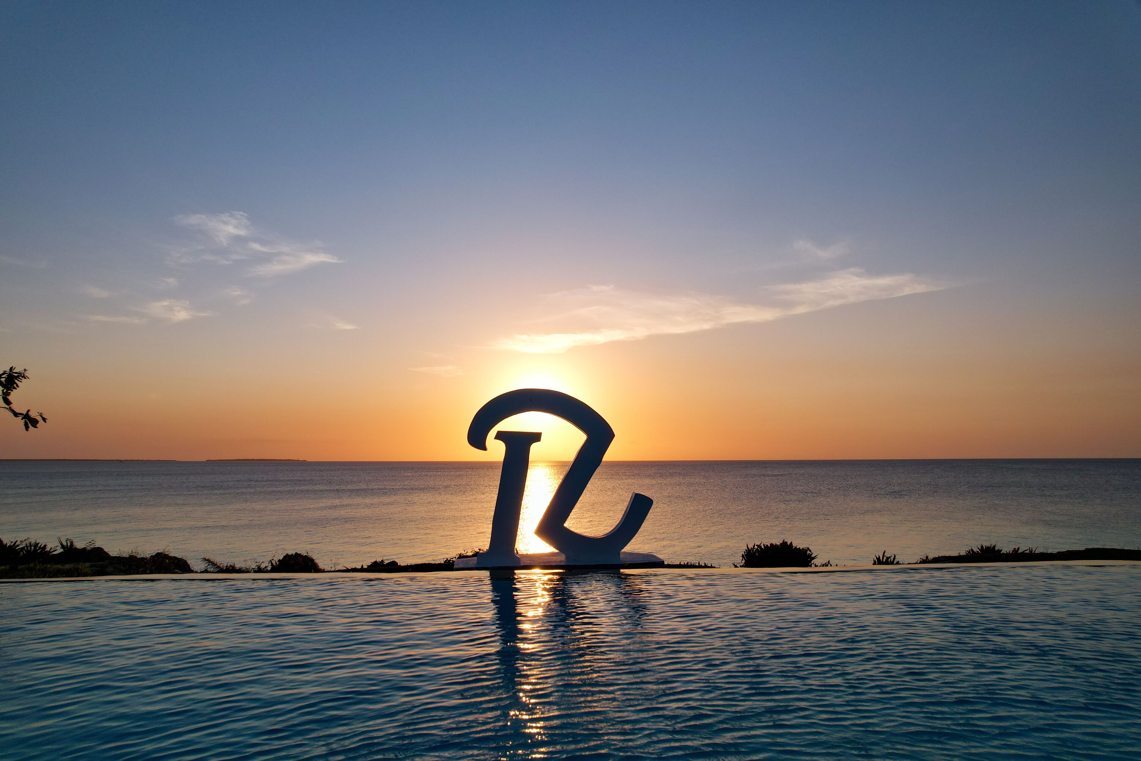 A sunset over a body of water with a large, abstract sculpture in the foreground.