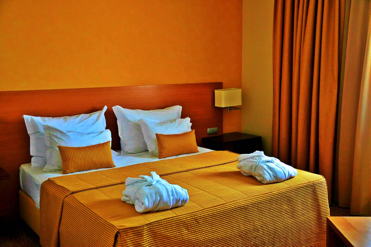 A hotel room with a large bed, two pillows, a nightstand with a lamp, and a window with curtains.