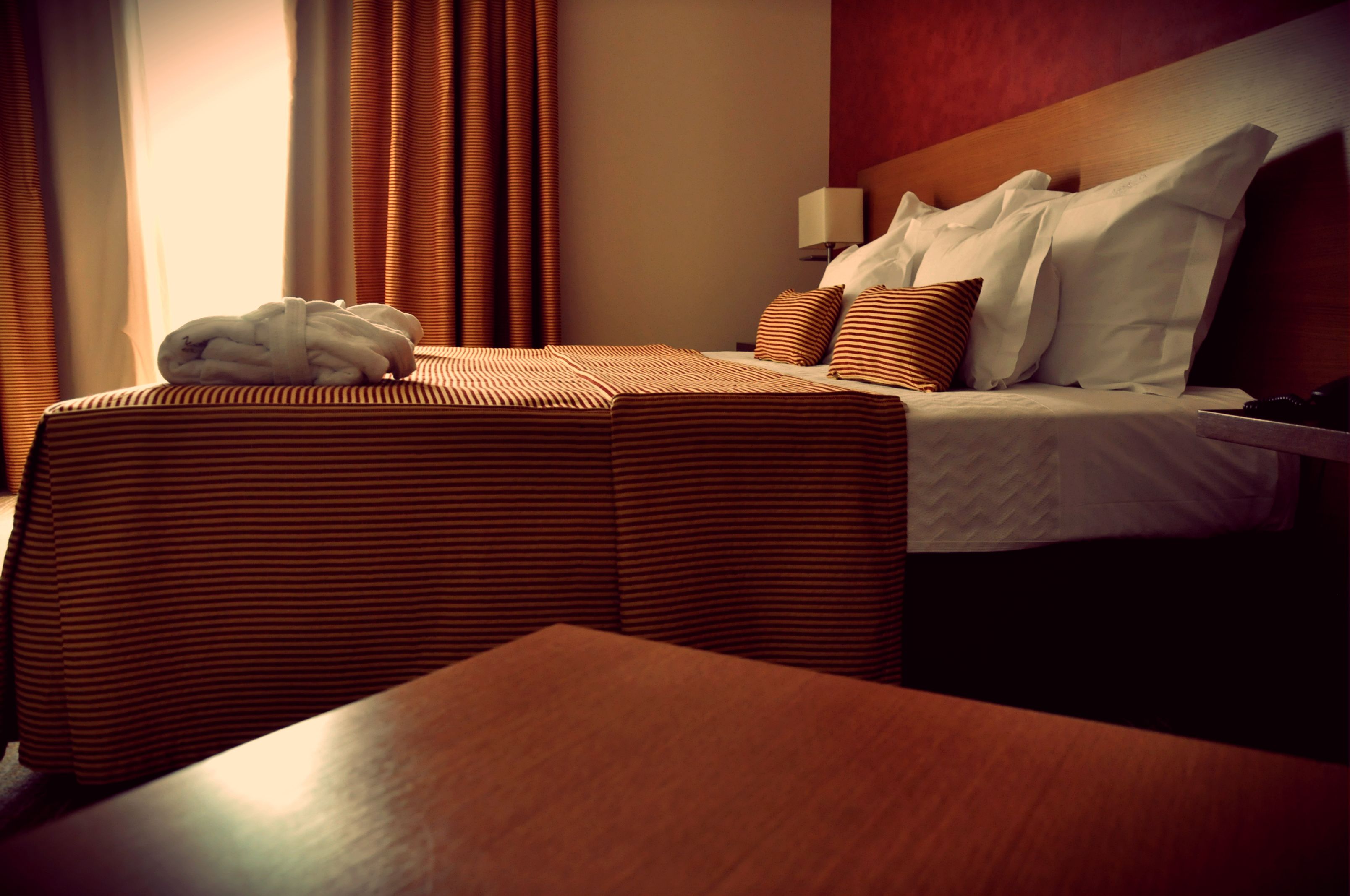 A hotel room with a bed, a bedside table, a lamp, and a window with curtains.