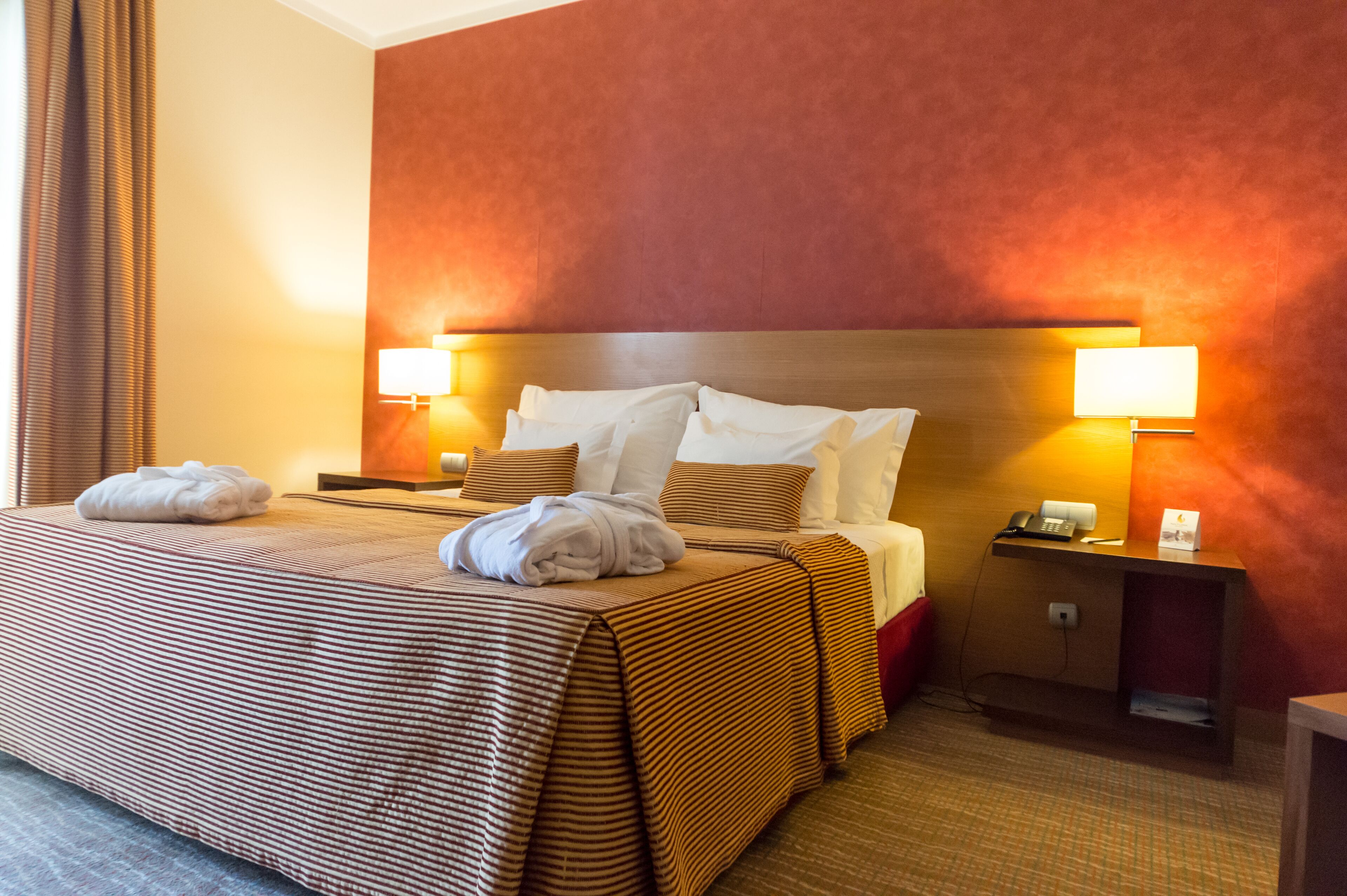 Hotellihuone, jossa on suuri sänky, kaksi yöpöytää valaisimineen, yökaappi ja punainen tehosteseinä.