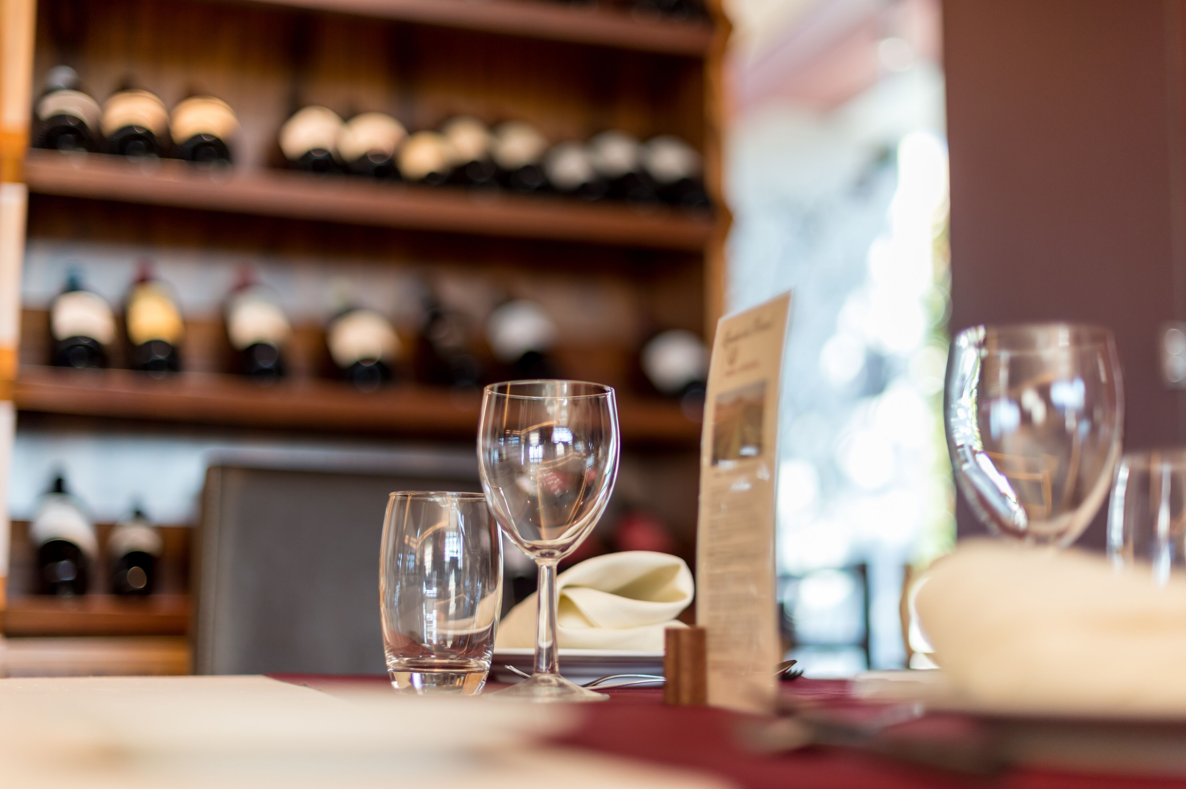 A restaurant setting with wine bottles on shelves, empty wine glasses, and a menu on the table.