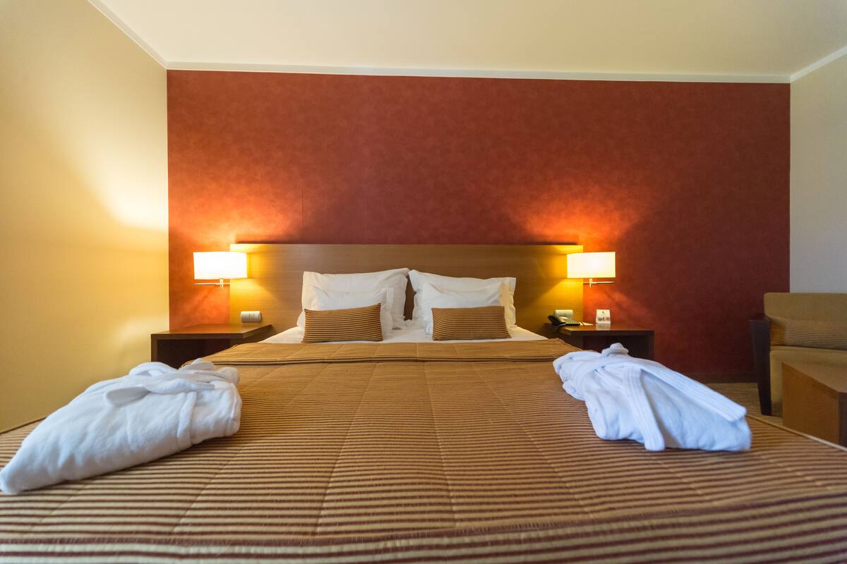 A hotel room with a large bed, two bedside lamps, and a brown striped bedspread.