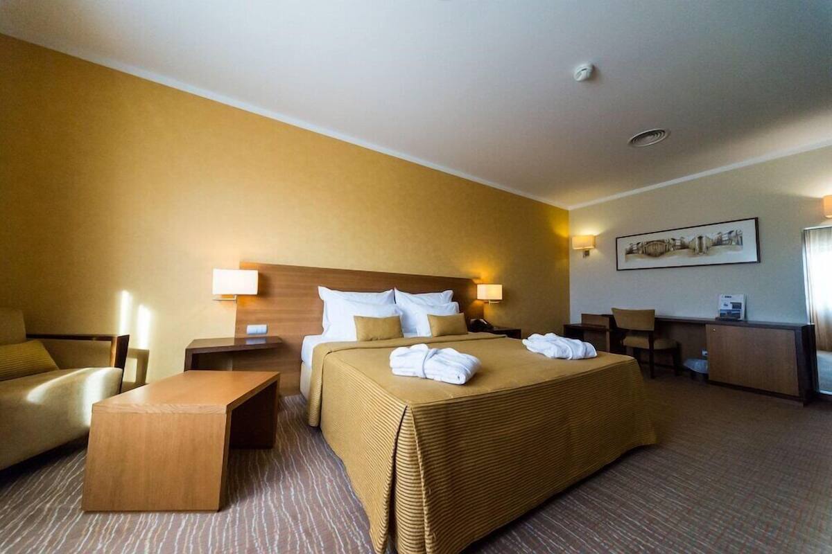 A hotel room with a bed, a desk, a chair, a sofa, and a lamp.