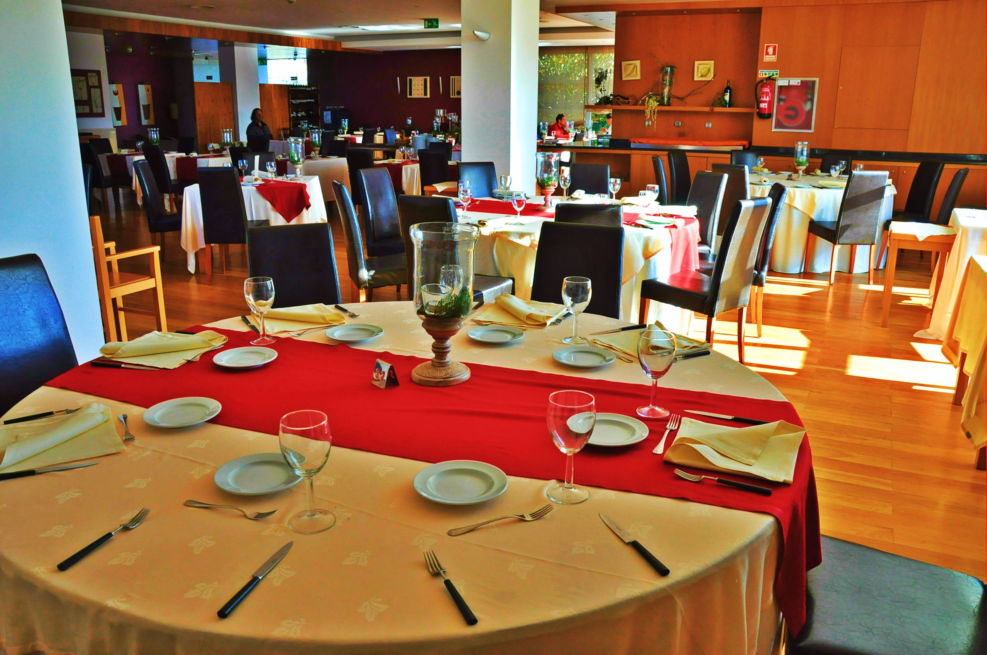 A restaurant with round tables set for dining, featuring red tablecloths and white plates.