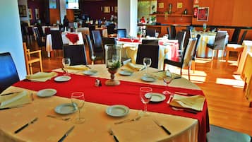 A restaurant with round tables set for dining, featuring red tablecloths and white plates.