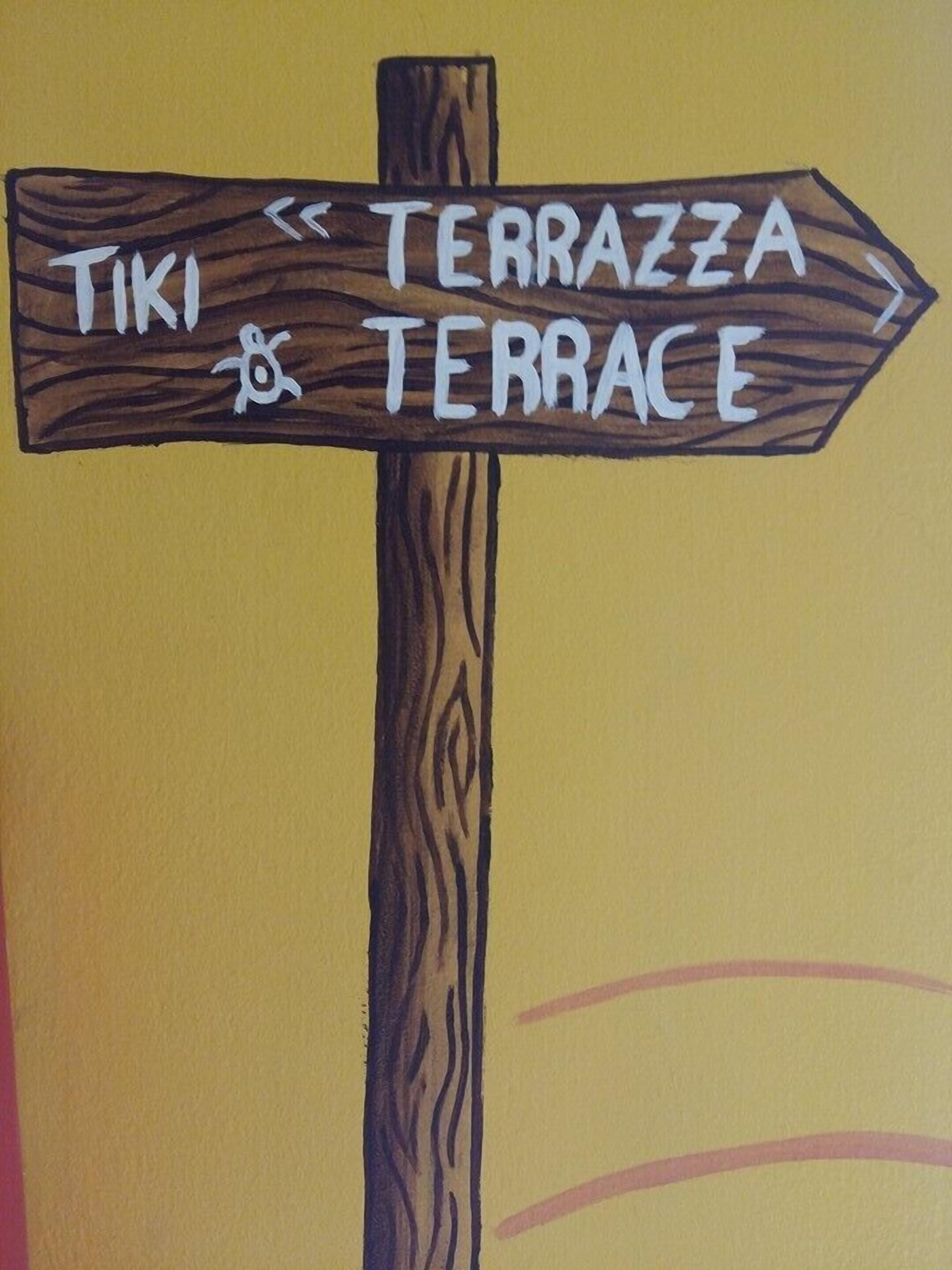 Un senyal de fusta amb fletxes que indiquen direccions cap a 'TIKI' i 'TERRAZZA'.