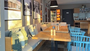 Een moderne eetruimte met een houten tafel en blauwe stoelen, een bank met kussens, en stadsgezichten in lijsten aan de muur.