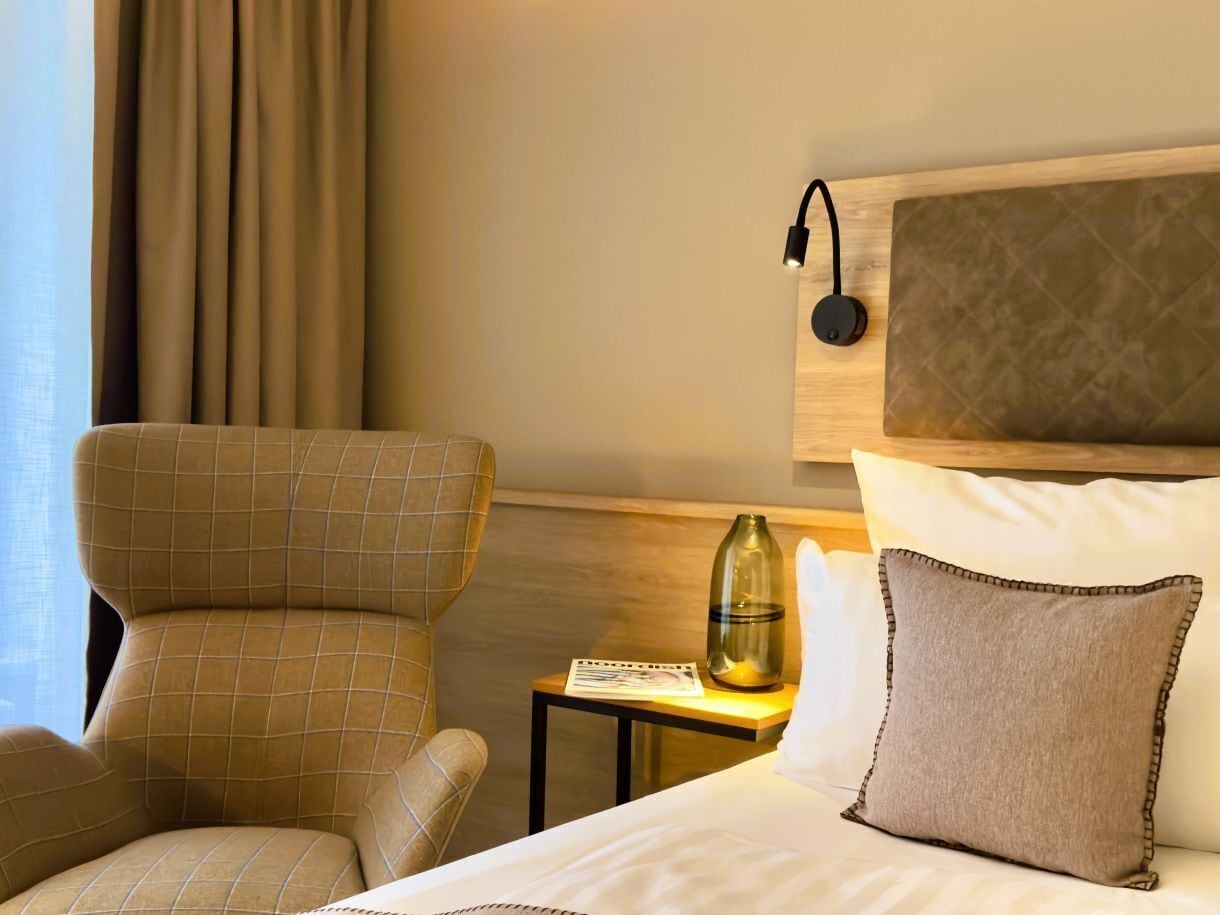 A hotel room with a bed, a chair, a nightstand, a lamp, and a window with curtains.
