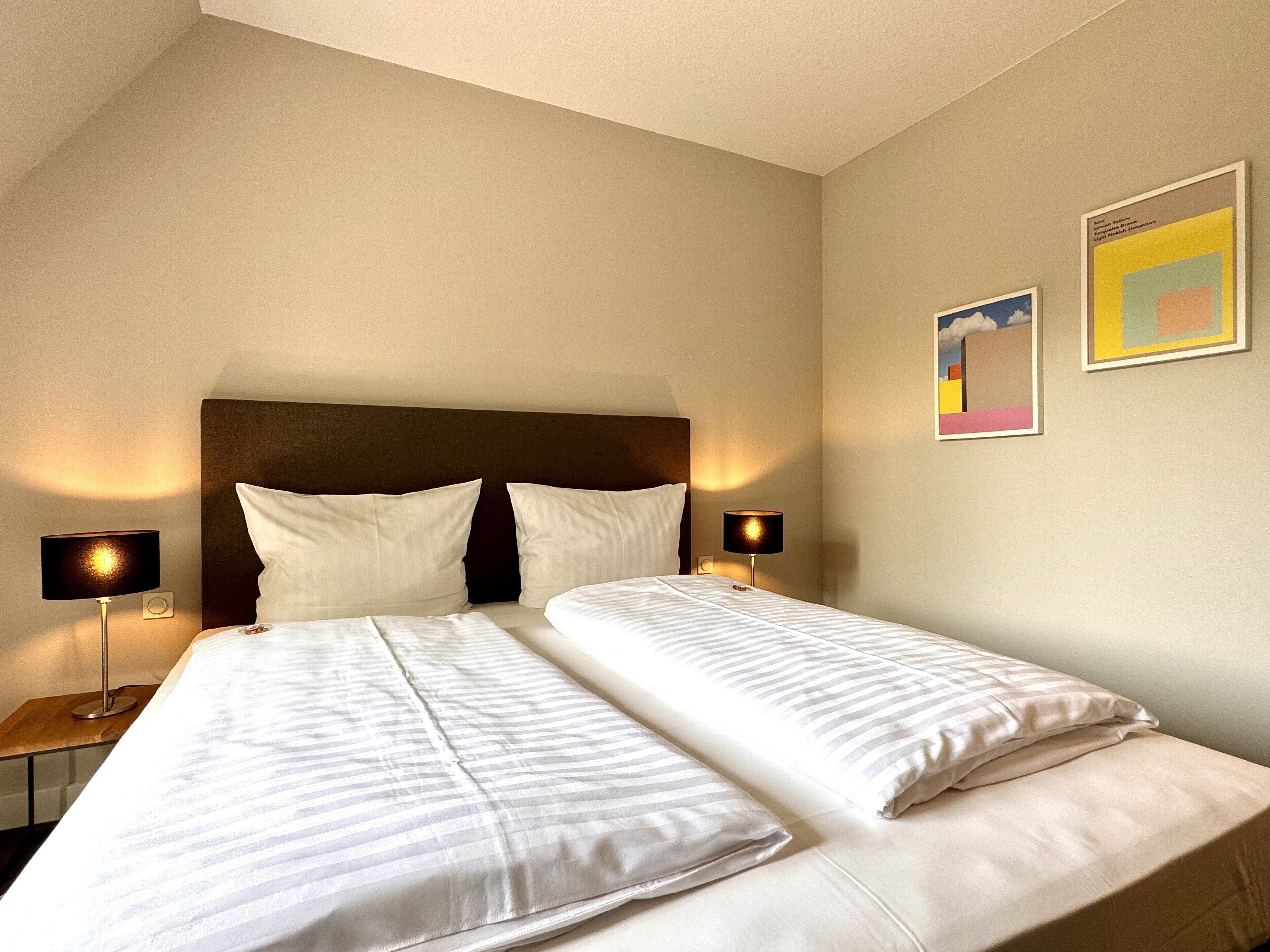Ett hotellrum med två sängar, en mörk sänggavel, sänglampor och två inramade konstverk på väggen.