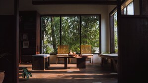 Quarto com uma janela grande, uma mesa de madeira, duas cadeiras e uma estante de livros.