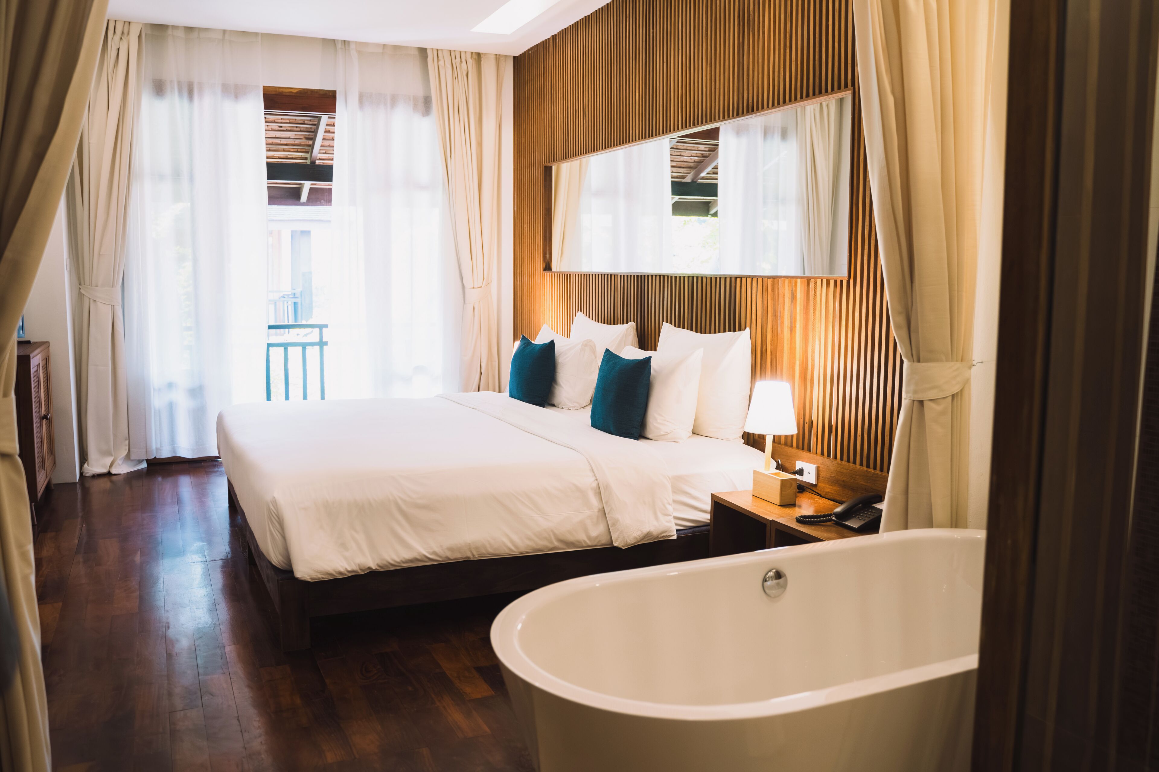 Ein Hotelzimmer mit einem großen Bett, einem hölzernen Kopfteil, einer Badewanne und einem großen Spiegel über dem Bett.