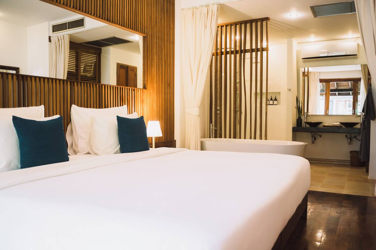 A hotel room with a large bed, a bathroom with a bathtub, and a mirror above the bed.