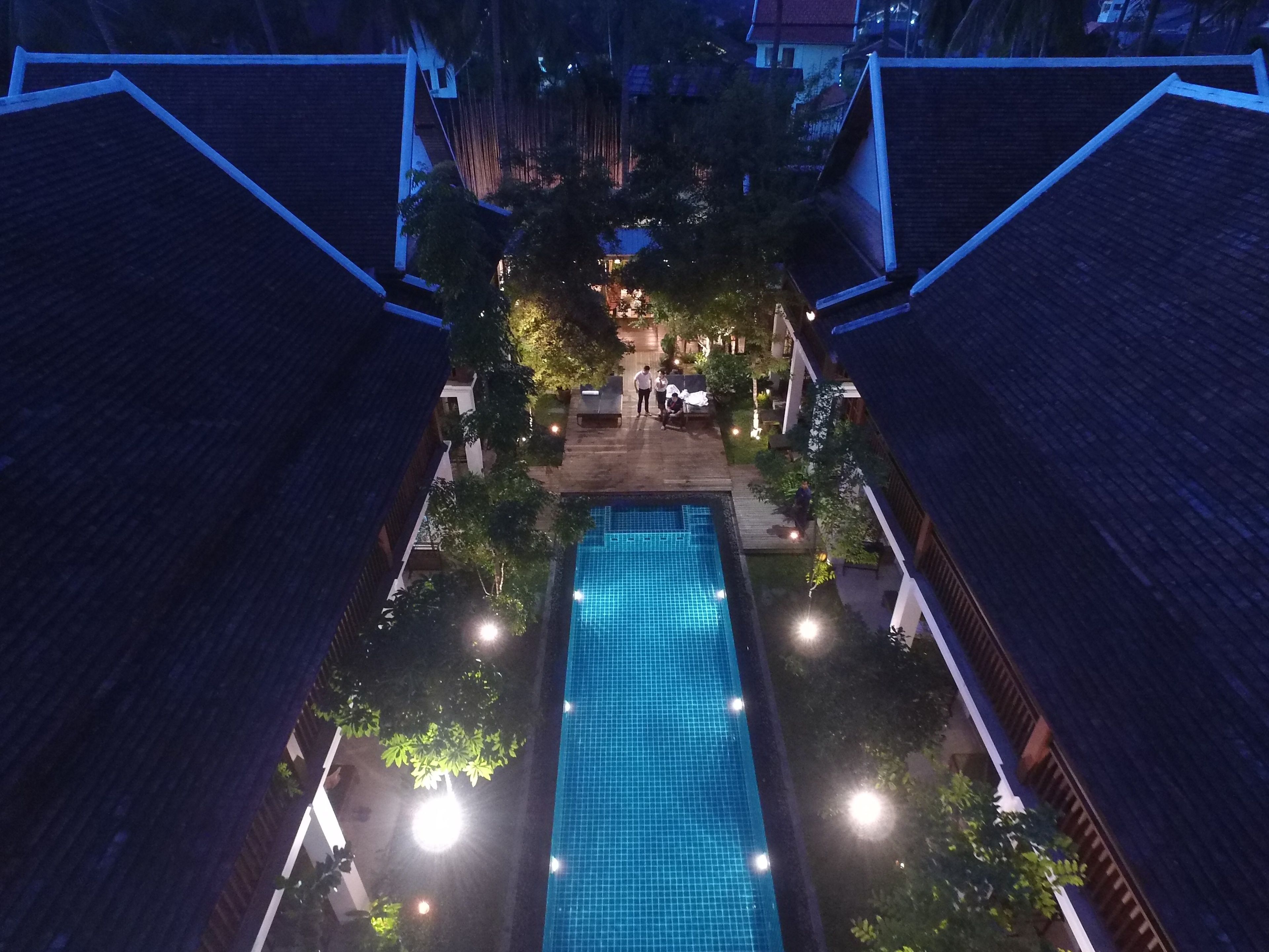 A rectangular swimming pool with a tiled surface, surrounded by a wooden deck and trees.