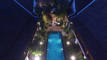 A rectangular swimming pool with a tiled surface, surrounded by a wooden deck and trees.