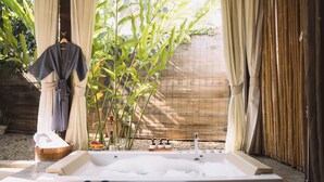 Uma área de spa com uma banheira grande, um banco de madeira e um roupão pendurado em um suporte.