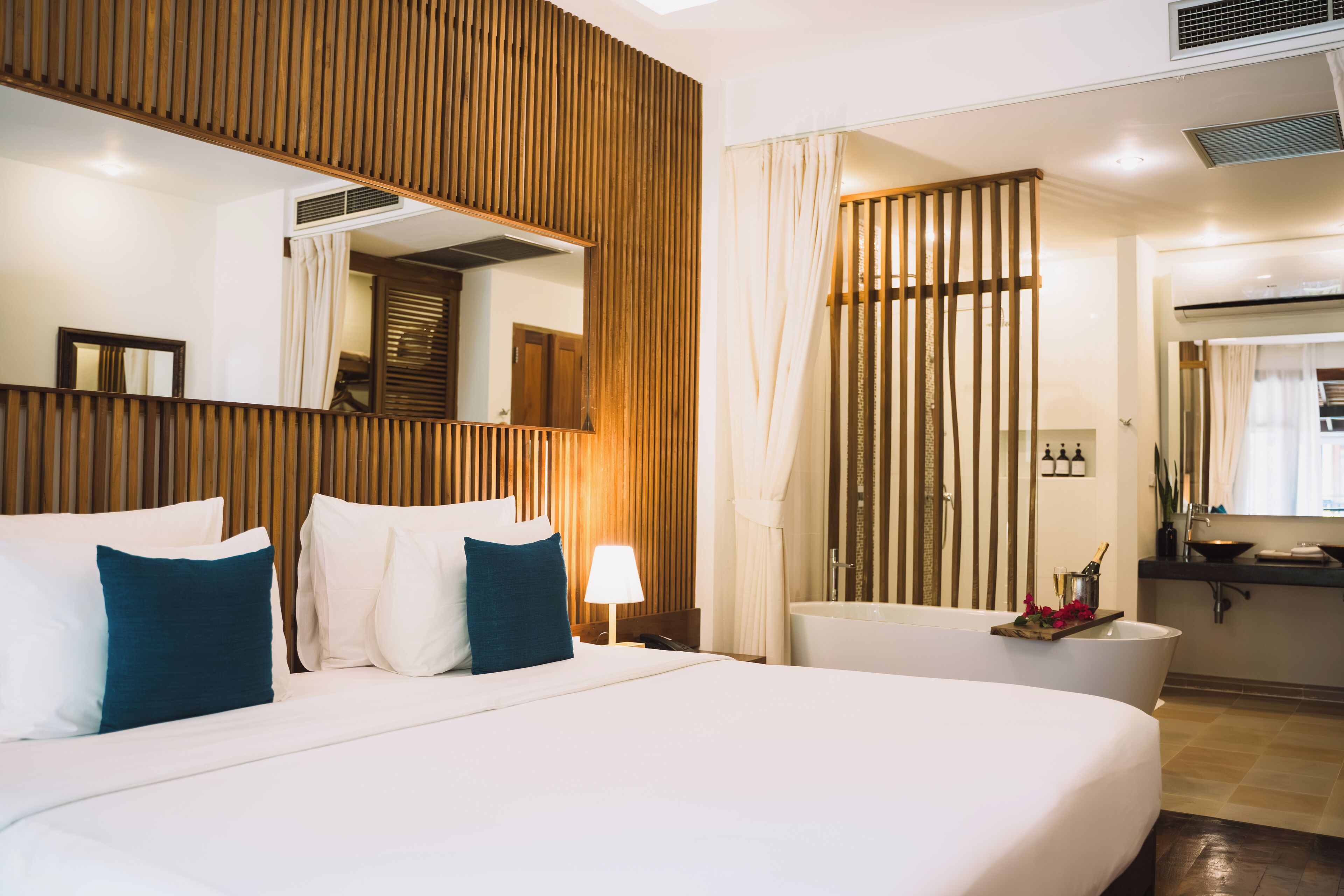 A hotel room with a large bed, a wooden headboard, a bathroom with a bathtub, and a mirror.