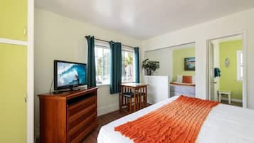 Une chambre d’hôtel avec un lit, un téléviseur posé sur une commode en bois, un bureau avec une chaise et une fenêtre avec des rideaux.