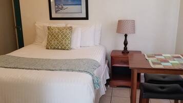 Habitación de hotel con cama, escritorio, silla, lámpara y un cuadro en la pared.