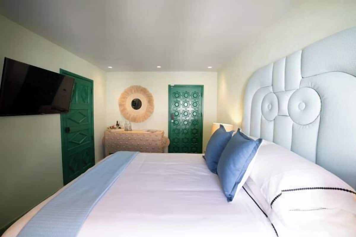 A bedroom with a bed, a television mounted on the wall, and two green doors.