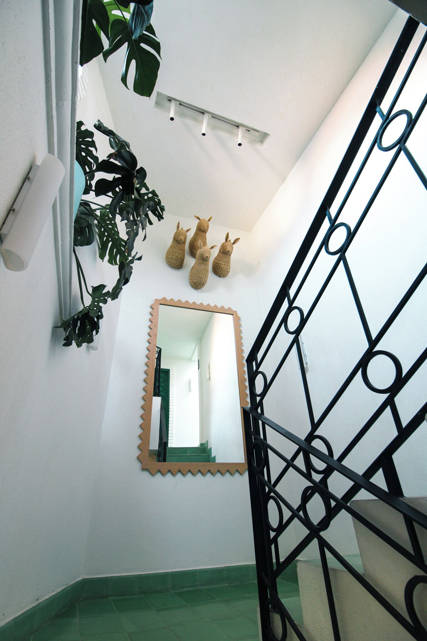 Eine Treppe mit schwarzem Metallgeländer, ein Spiegel mit geschnitztem Rahmen und ein grün gefliester Boden.