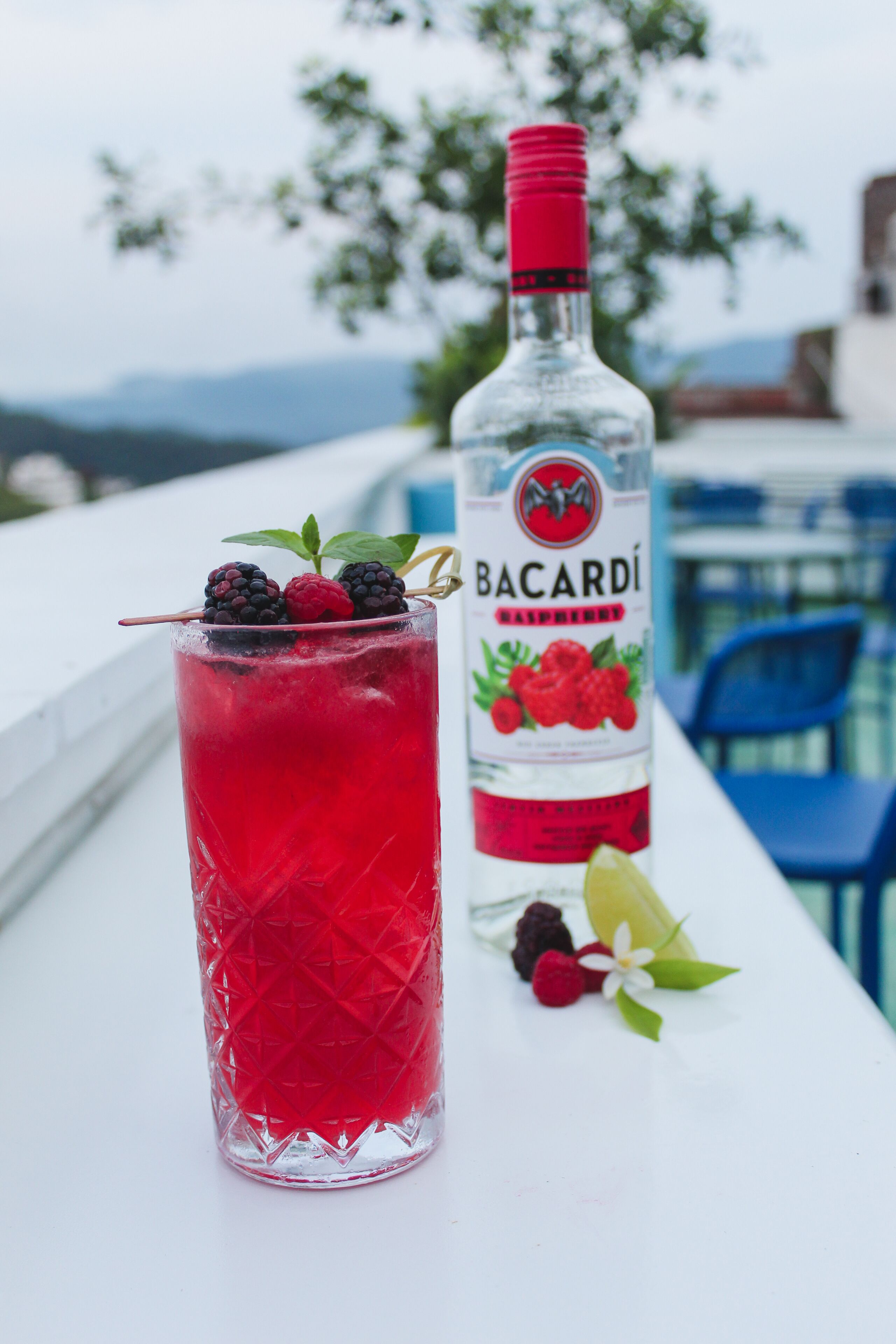 Un vaso de bebida roja con zarzamoras y una botella de Bacardí Frambuesa.