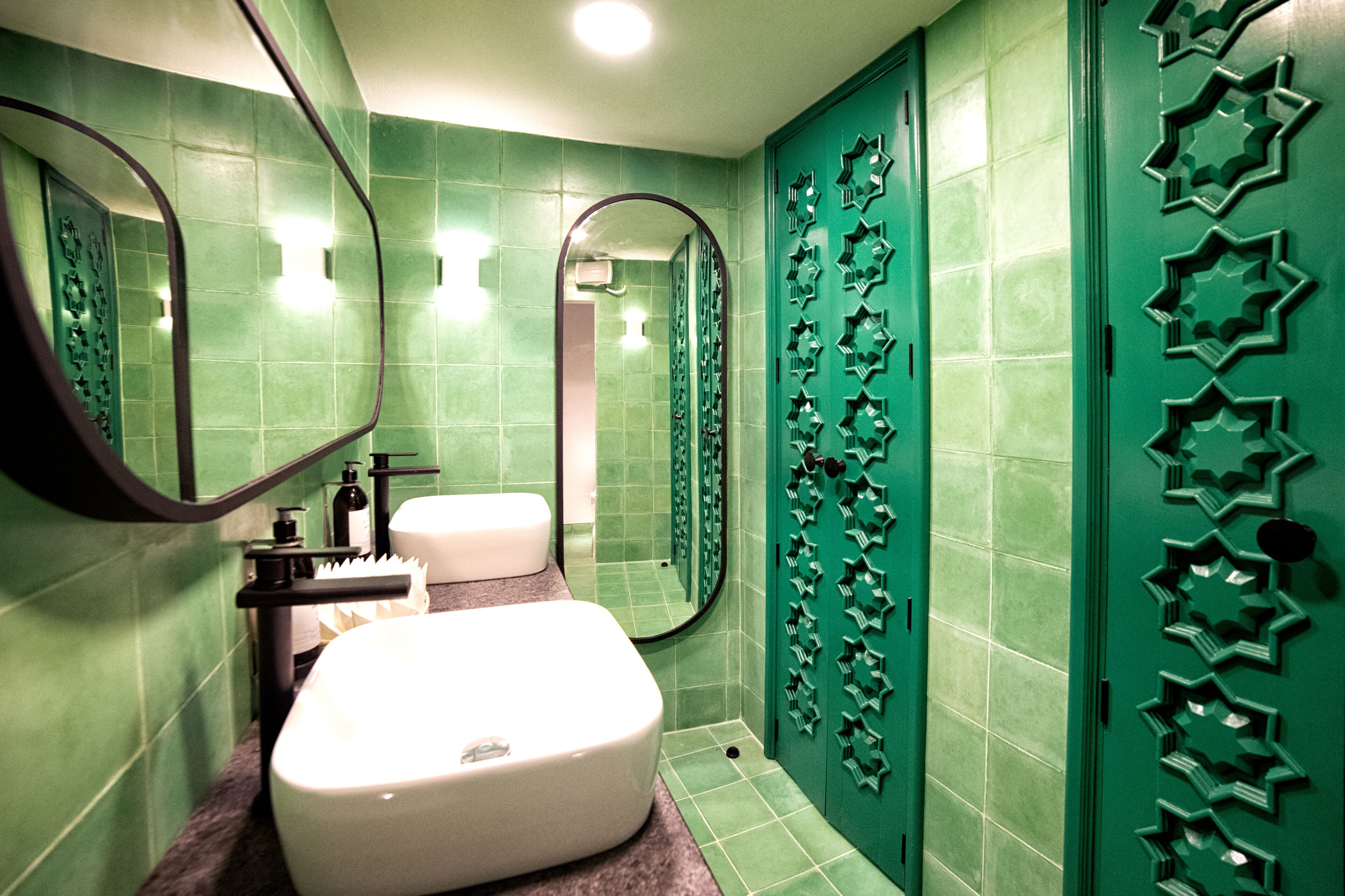 A bathroom with green tiles, a white sink, a mirror, and a shower area.