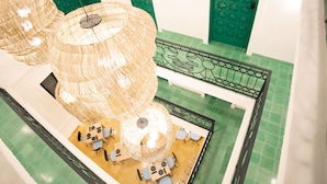 Un espacio interior amplio con pisos de baldosas verdes, una zona central de estar con mesas y sillas, y barandillas decorativas de metal.
