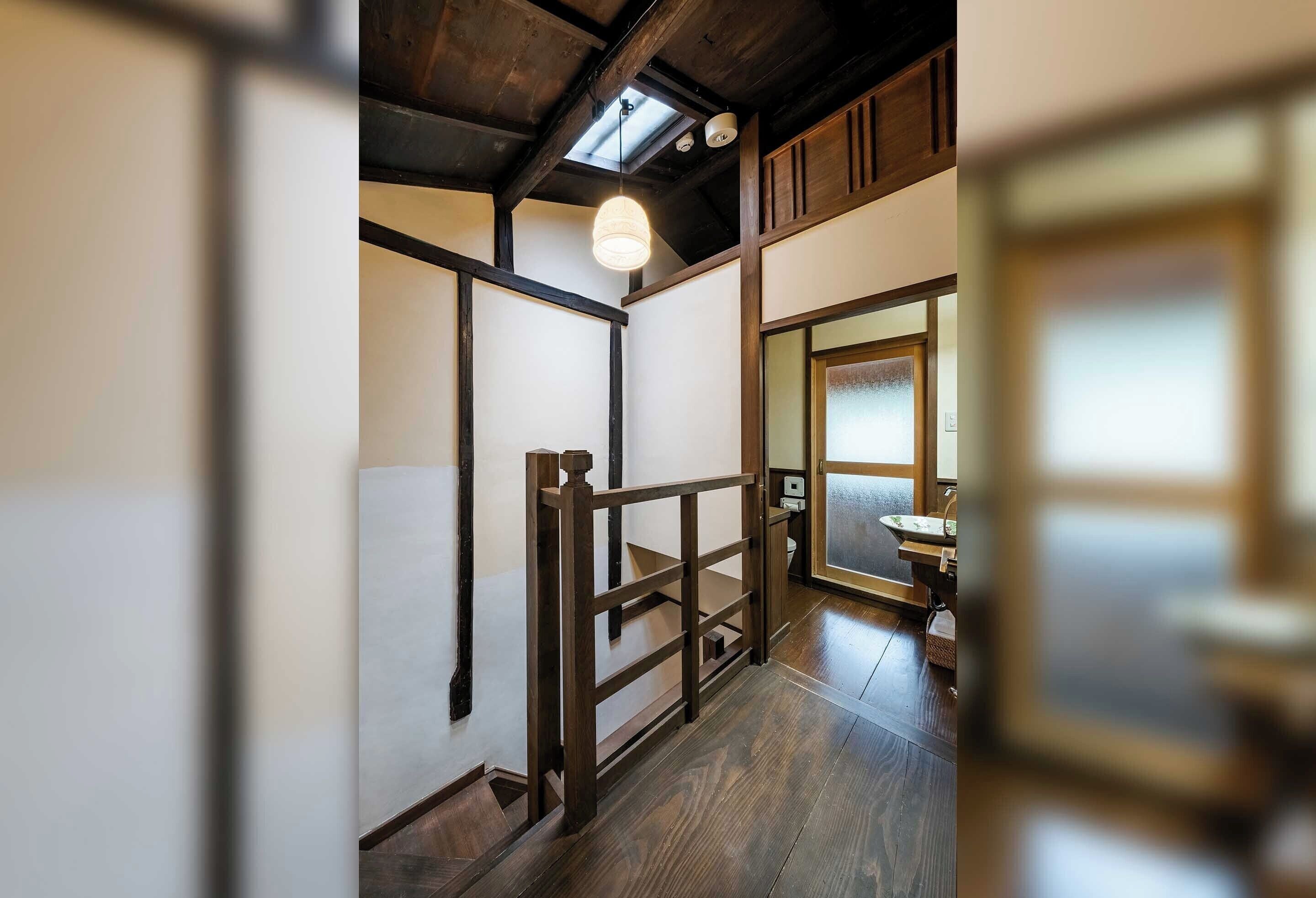 A traditional Japanese interior with tatami flooring, a wooden staircase, and a sliding door leading to a washbasin area.