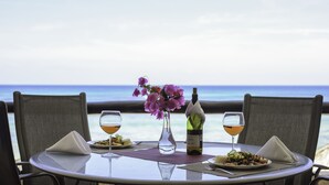 Mesa para dos con vista al océano, una botella de vino y un jarrón de flores.