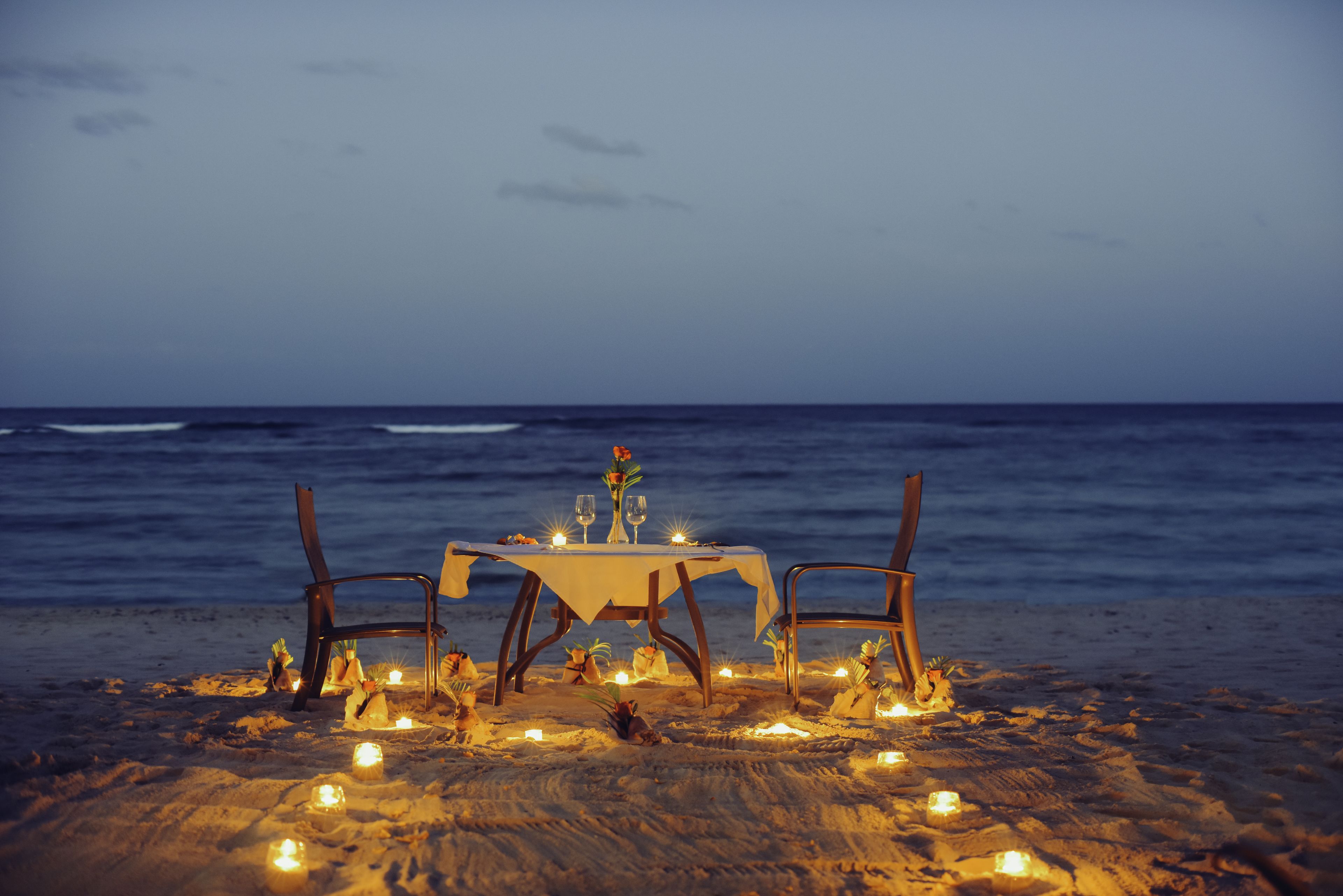 Ein Abendessen am Strand mit Tisch, Stühlen, Kerzen und Meerblick.