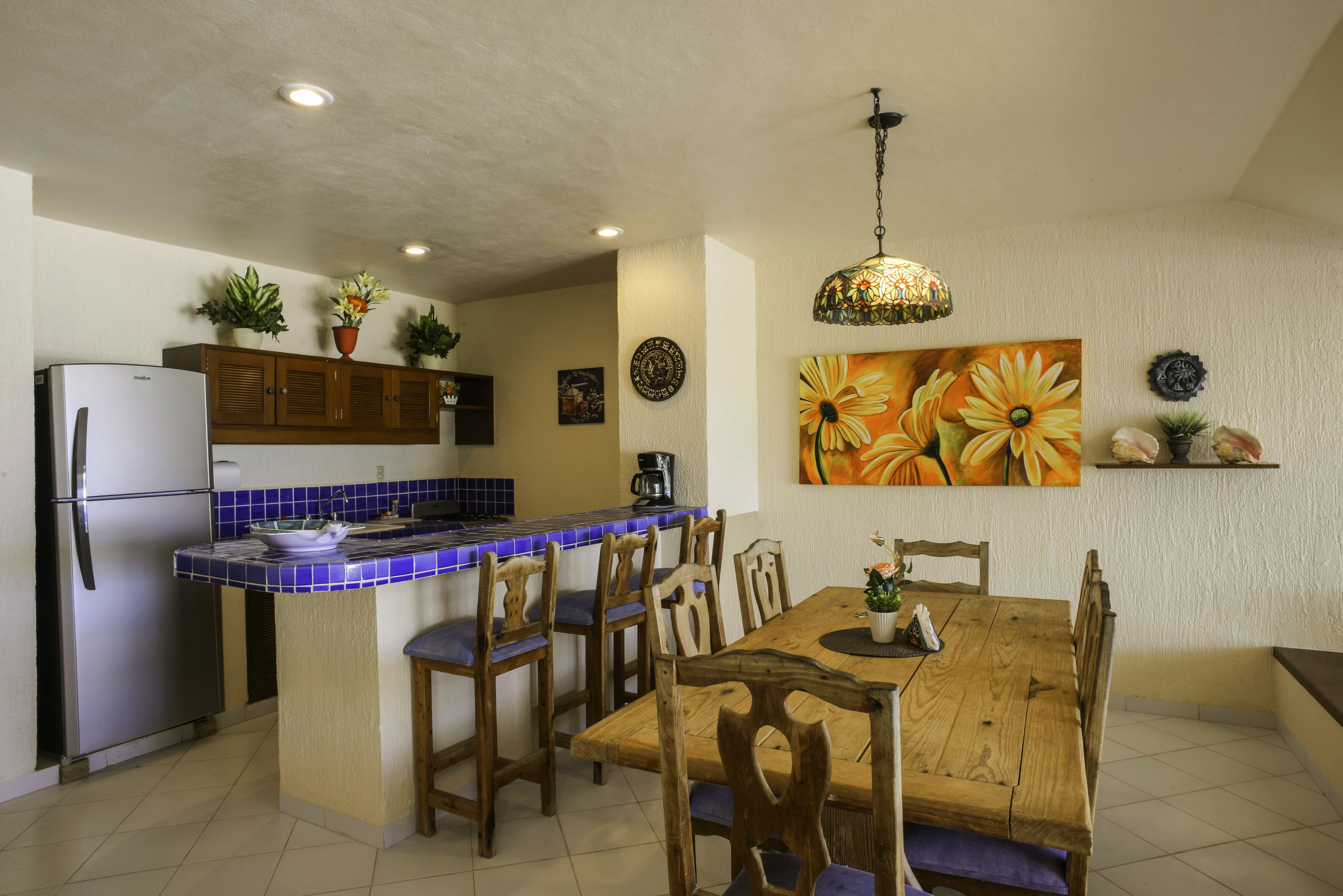 A kitchen with a wooden dining table, chairs, a refrigerator, and a blue-tiled island.