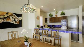 A kitchen with a blue-tiled backsplash, wooden chairs, a dining table with a white orchid, and a refrigerator.