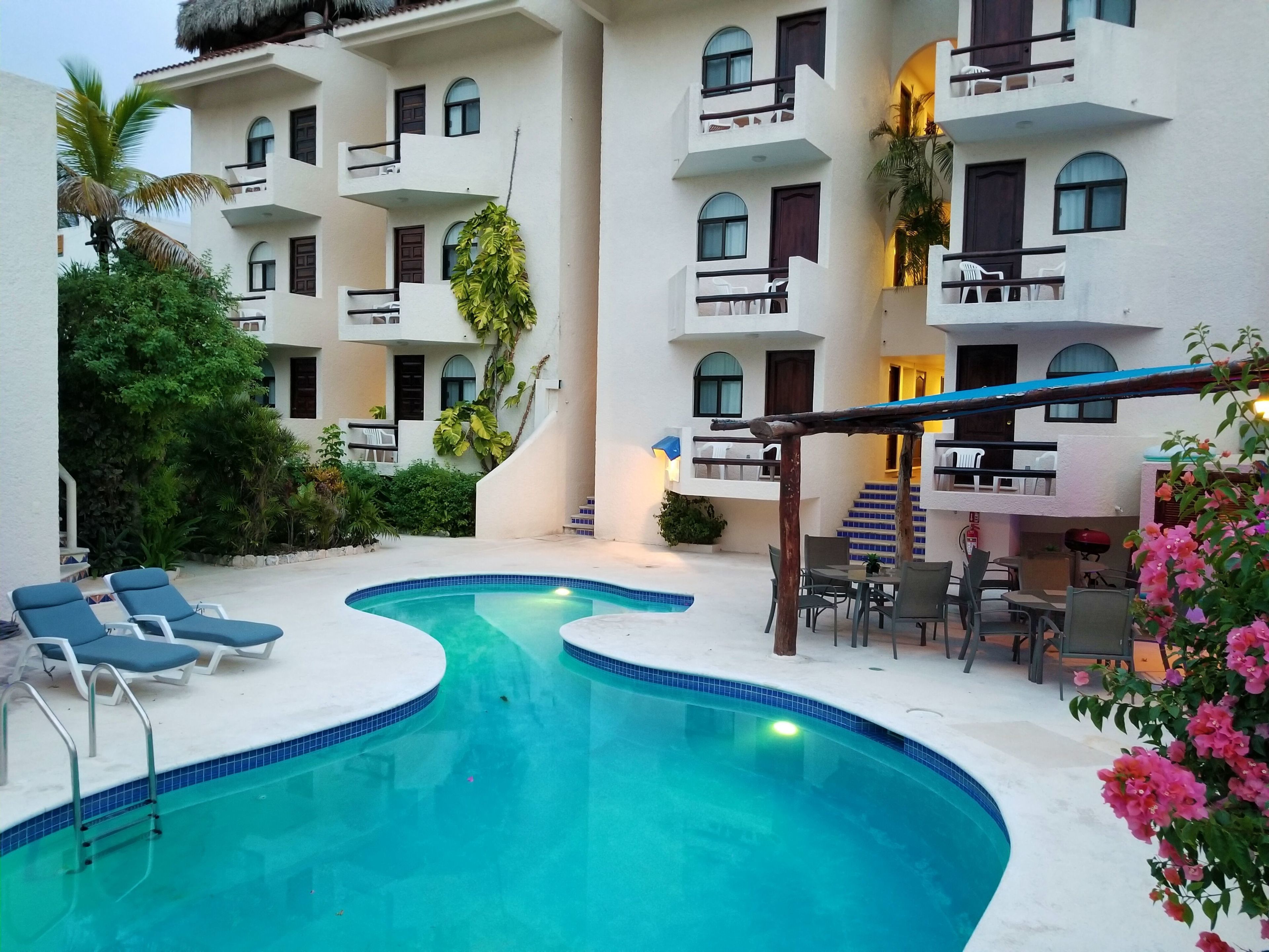 A pool area with lounge chairs and a small table, surrounded by a building with balconies and a staircase.