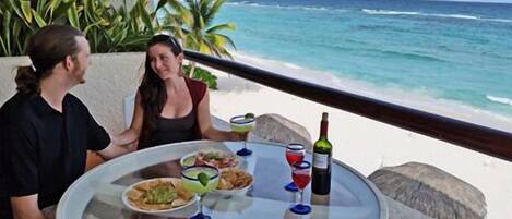 A table with food and drinks, overlooking a beach and ocean.