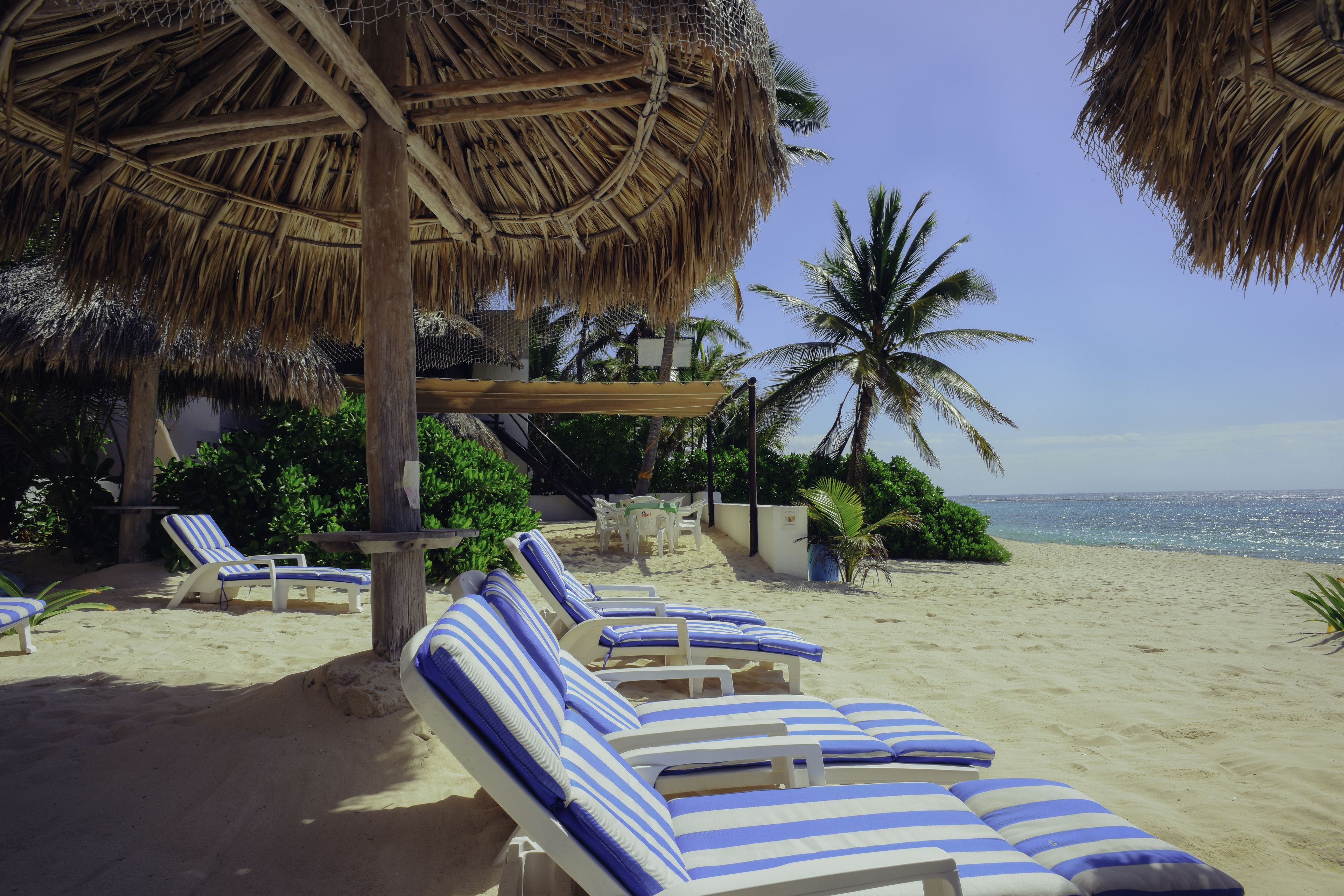 A beachside lounge area with striped lounge chairs and a thatched roof structure.