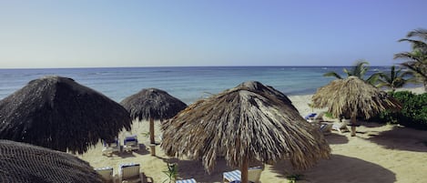 Une plage avec des parasols en chaume, des chaises longues et une vue dégagée sur l’océan.