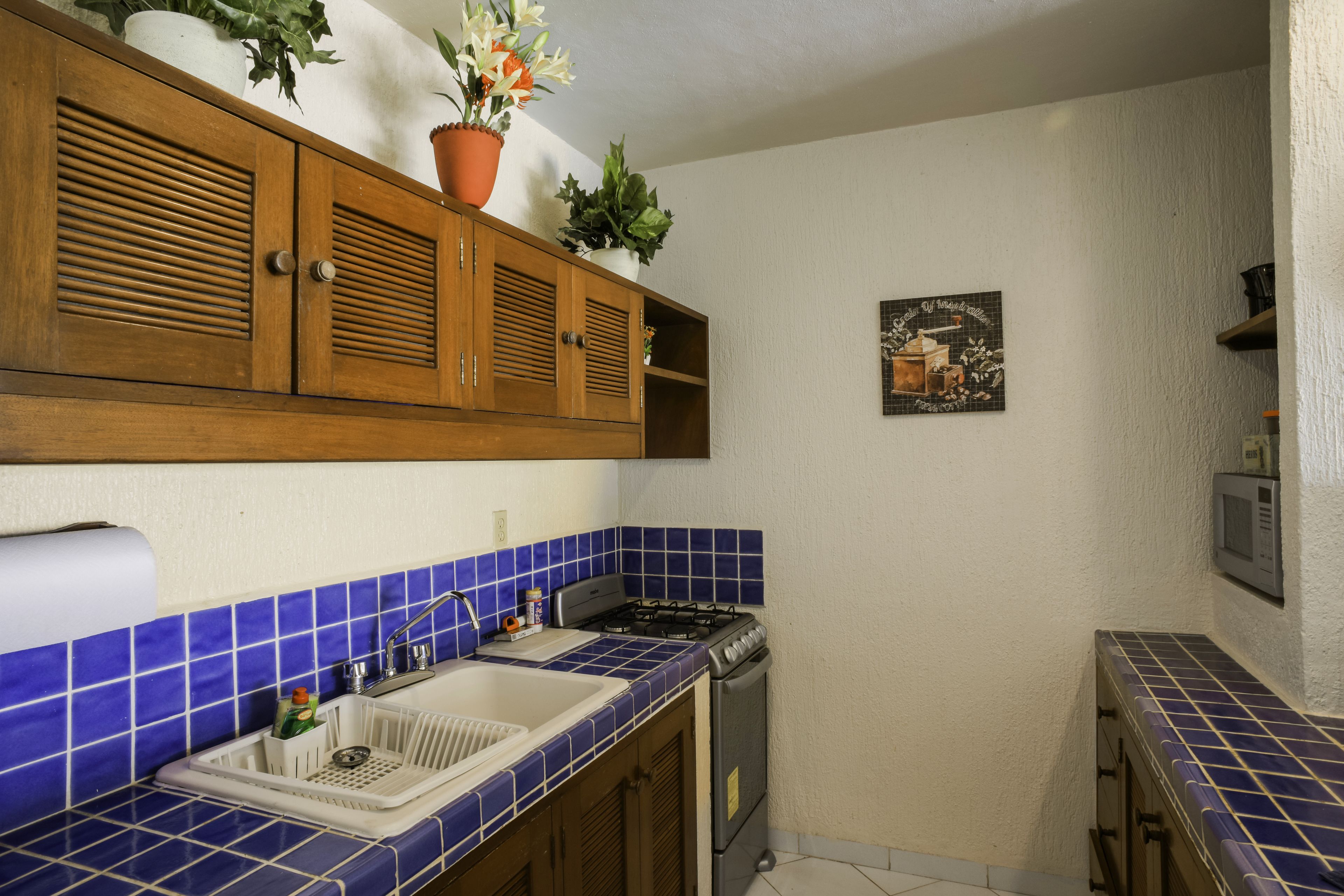 Uma cozinha com painel de azulejos azuis, armários de madeira, fogão a gás e uma pia.